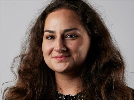 Smiling woman with long curly hair looking at the camera against a plain background.