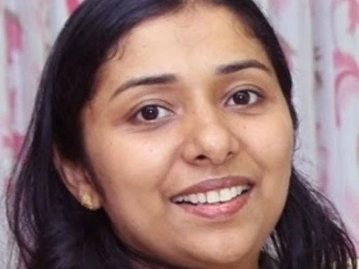 Close-up of a woman smiling in front of pink and white floral curtains.