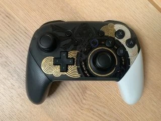Nintendo Switch Pro Controller with a custom gold and black design placed on a wooden table.