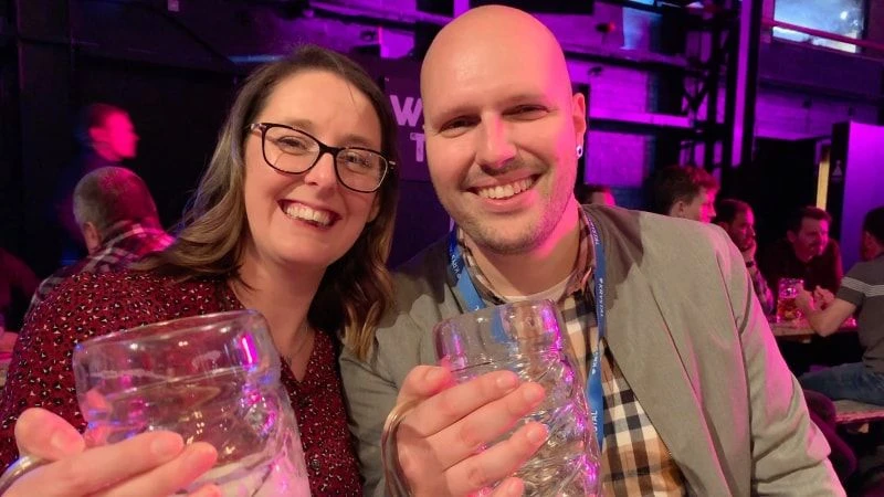 A man and a woman holding empty beer glasses and smiling broadly.